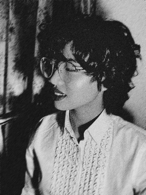 A photo of Fiona, an Asian woman, with her head turned to the left. She has wire-frame glasses and curly hair. The image has been processed with Photoshop to induce a sepia tone, noise, and a motion-blurred background.